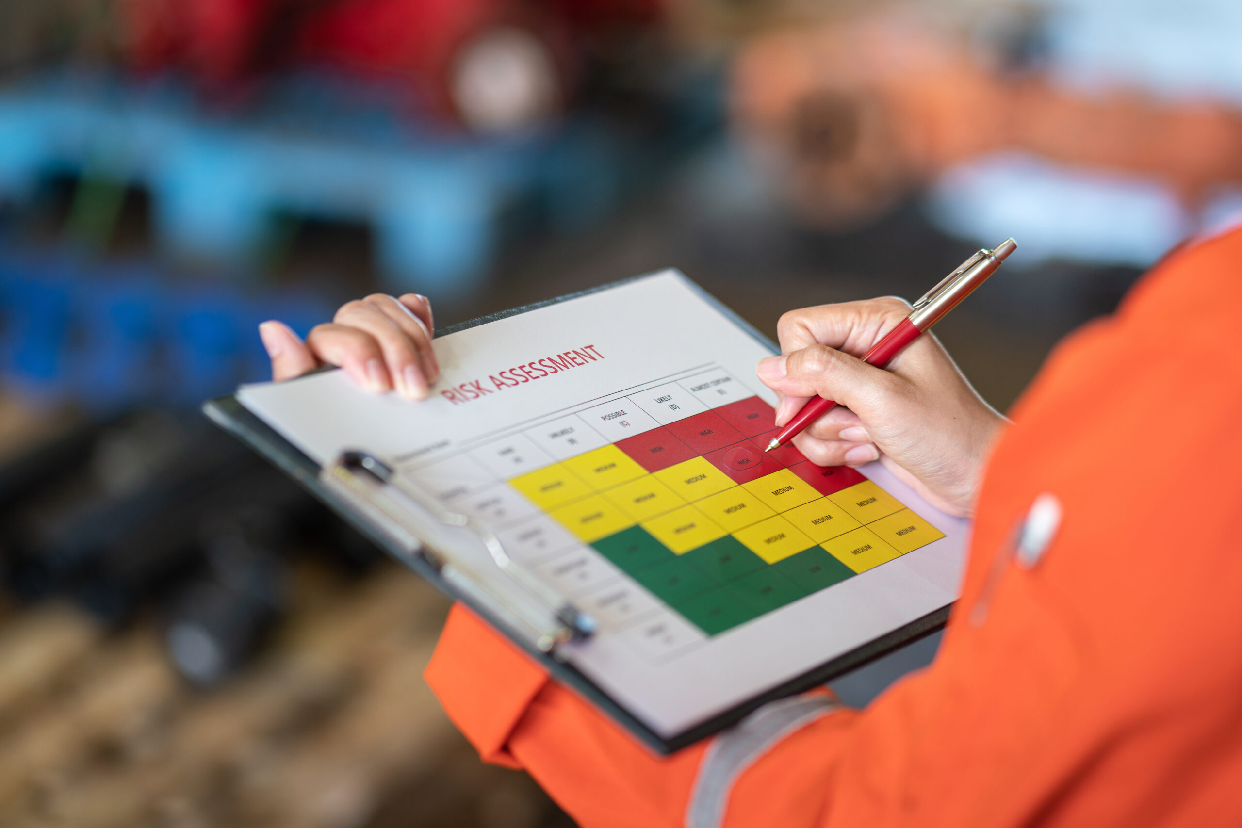 A person is holding a pen and getting ready to mark a piece of paper held on a clipboard. That piece of paper features a diagram that says 'Risk Assessment.'